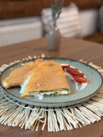 Two golden-brown crepes folded with cheese filling, served on a blue plate with cherry tomato slices nearby.