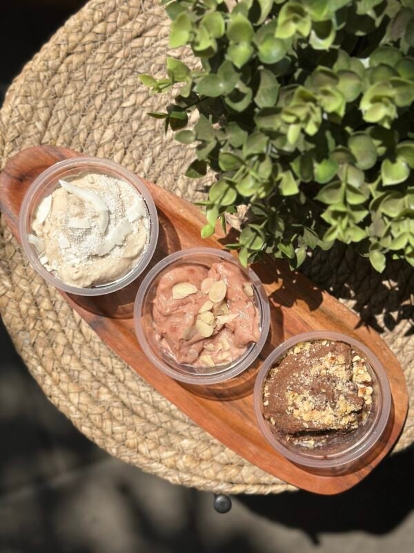 Top-down view of four cups of ice cream with toppings on a wooden board beside a green plant.