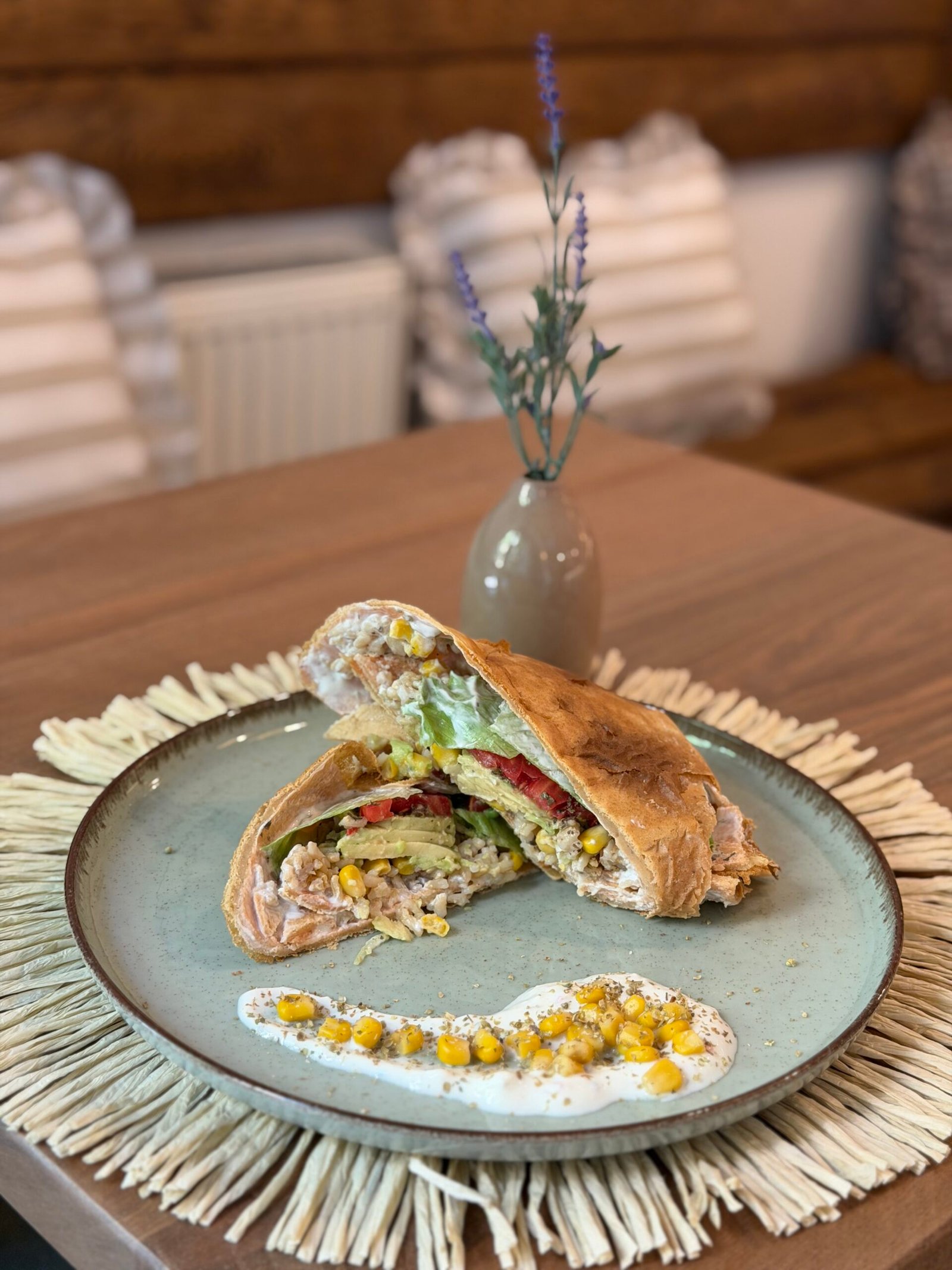 1786440188575103 Crusty sandwich filled with corn, lettuce and peppers on a blue plate, with a creamy corn dip beside it on a rustic table.