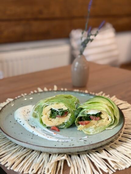 Green veggie wraps filled with greens and tomatoes on a blue plate with a white drizzle, set on a woven placemat.